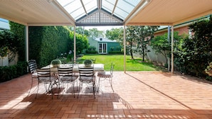 Une terrasse couverte avec un sol en briques et une table entourée de chaises.