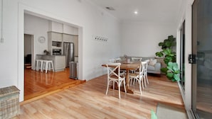 Une cuisine moderne avec des meubles blancs, un réfrigérateur en acier inoxydable et un coin repas comprenant une table en bois et des chaises blanches.