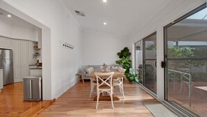 Une cuisine moderne avec des meubles blancs, une table à manger en bois et une porte-fenêtre coulissante donnant sur un espace extérieur.