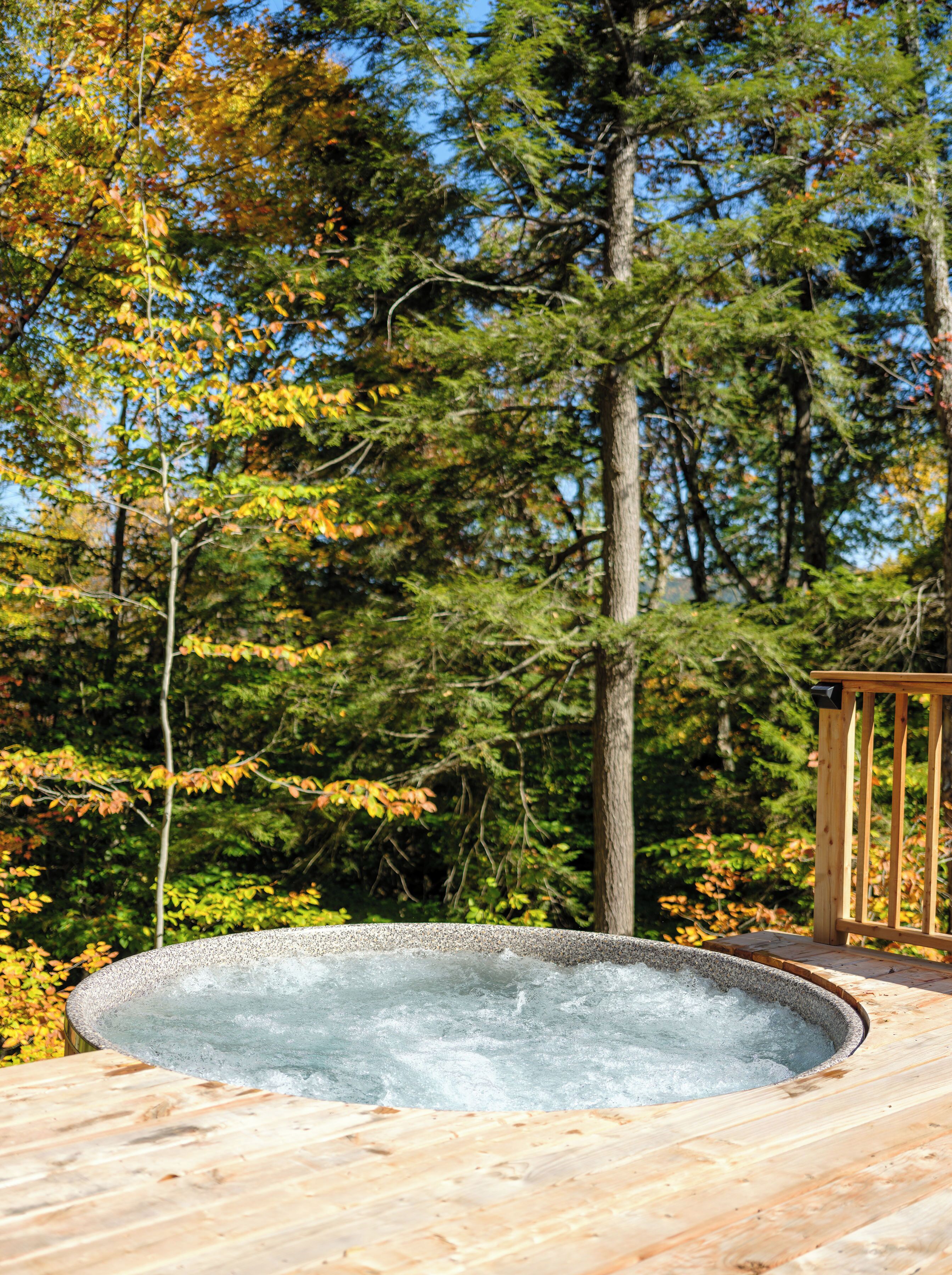 Un bain à remous sur une terrasse en bois, entouré d’arbres.