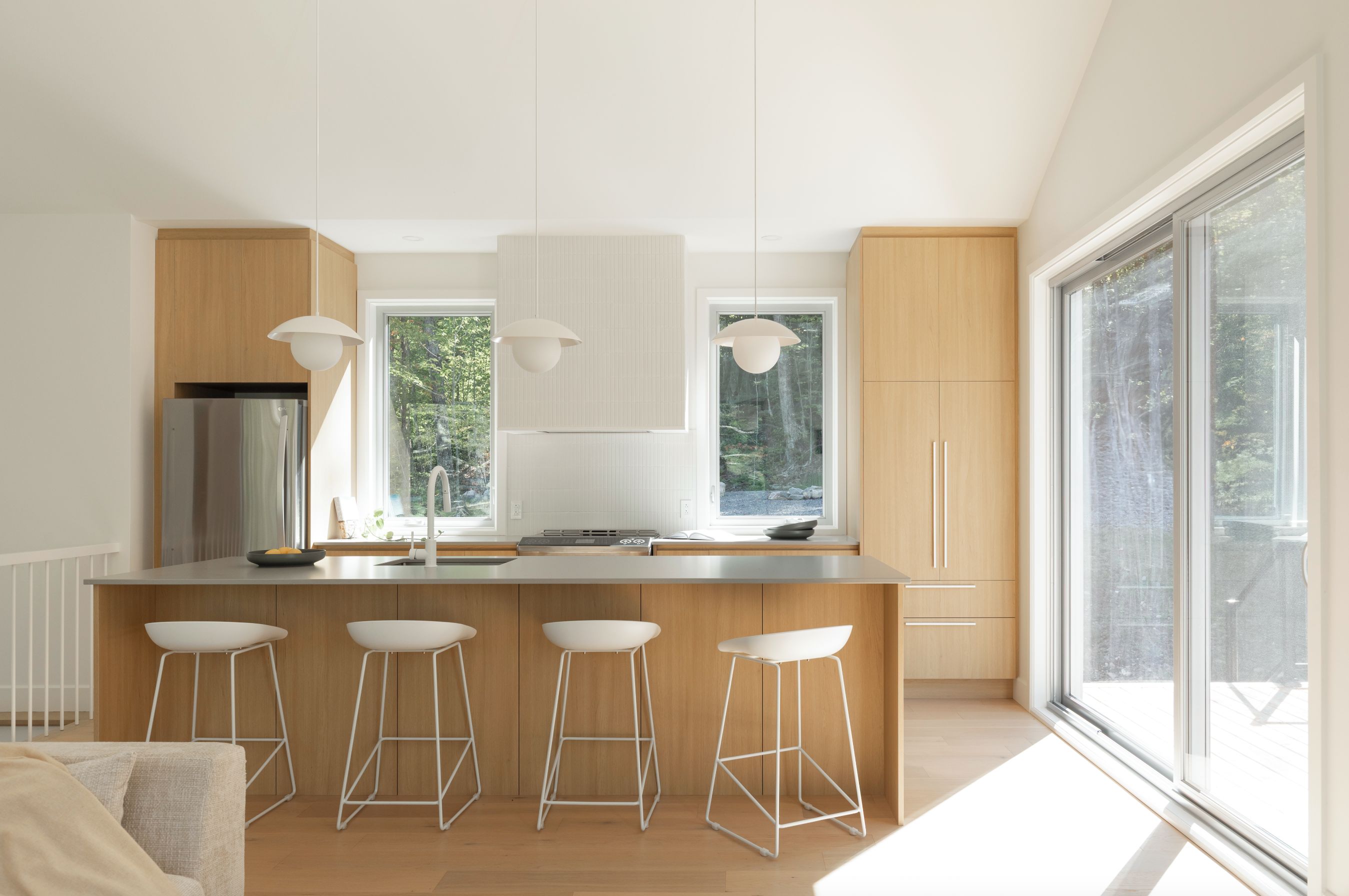 Une cuisine moderne dotée d’un îlot central, de tabourets de bar, de luminaires suspendus et de grandes fenêtres.