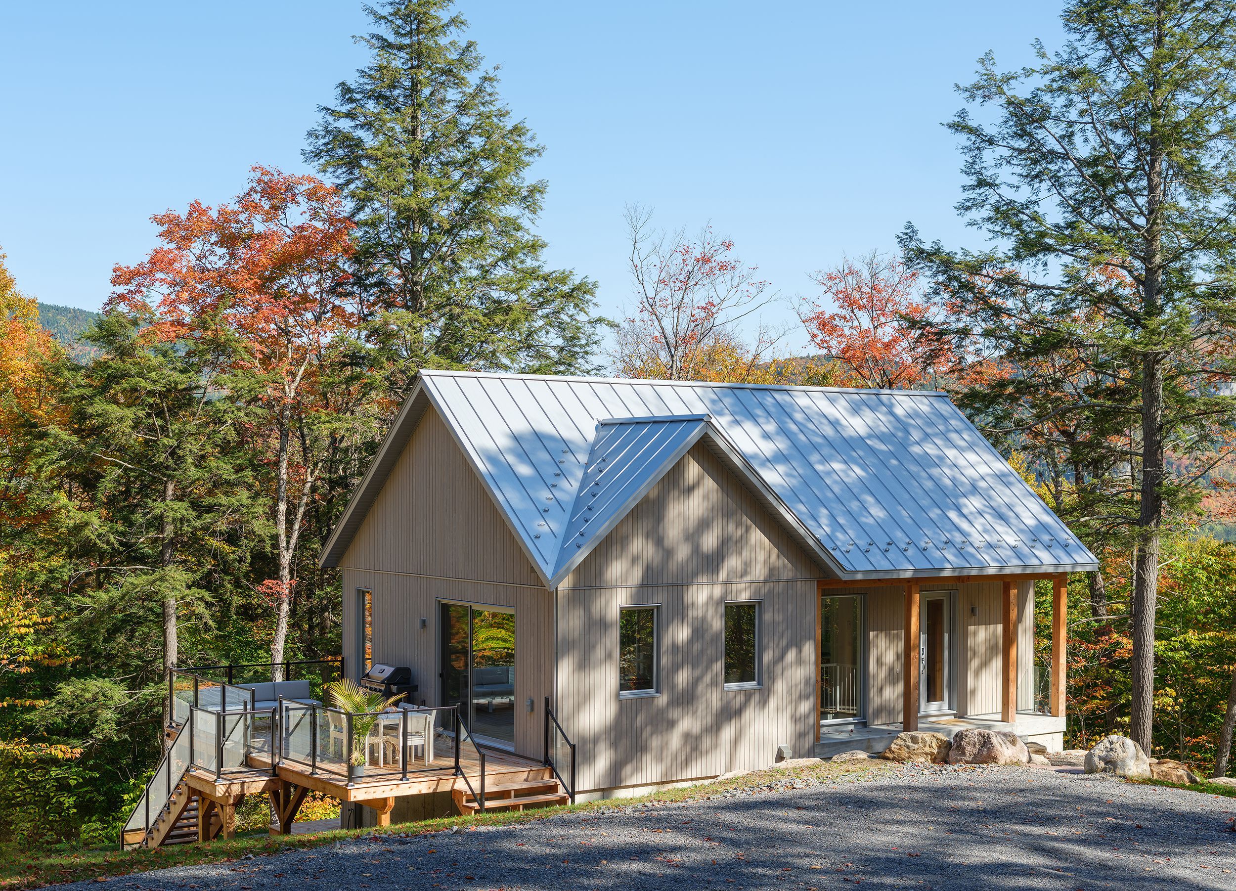 A cabin with a metal roof, wooden deck, and a view of the surrounding forest.