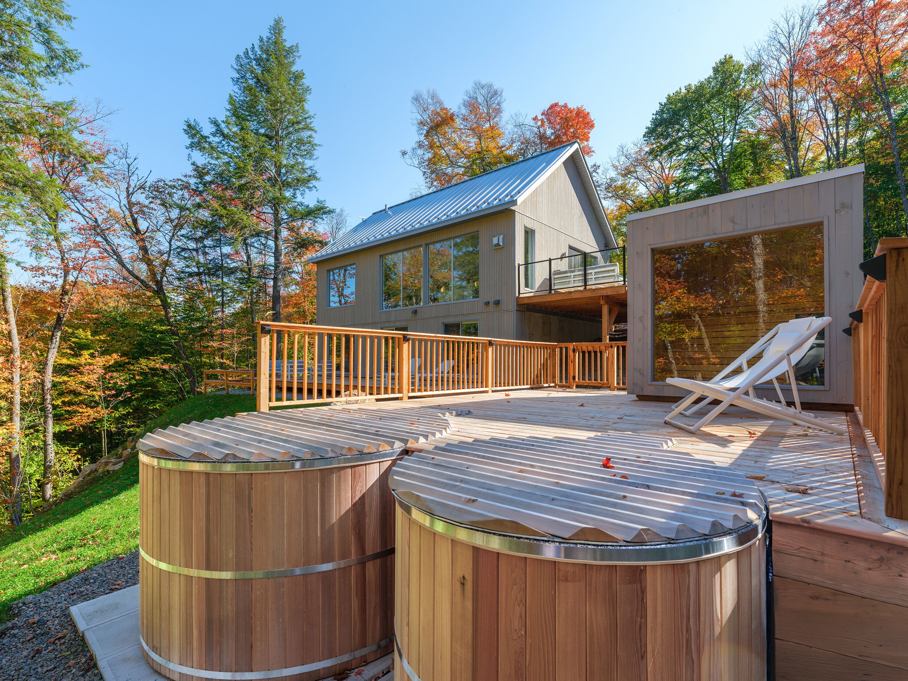 A modern house with a deck, two wooden hot tubs, and a hot tub on the side.