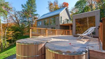 A modern house with a deck, two wooden hot tubs, and a hot tub on the side.