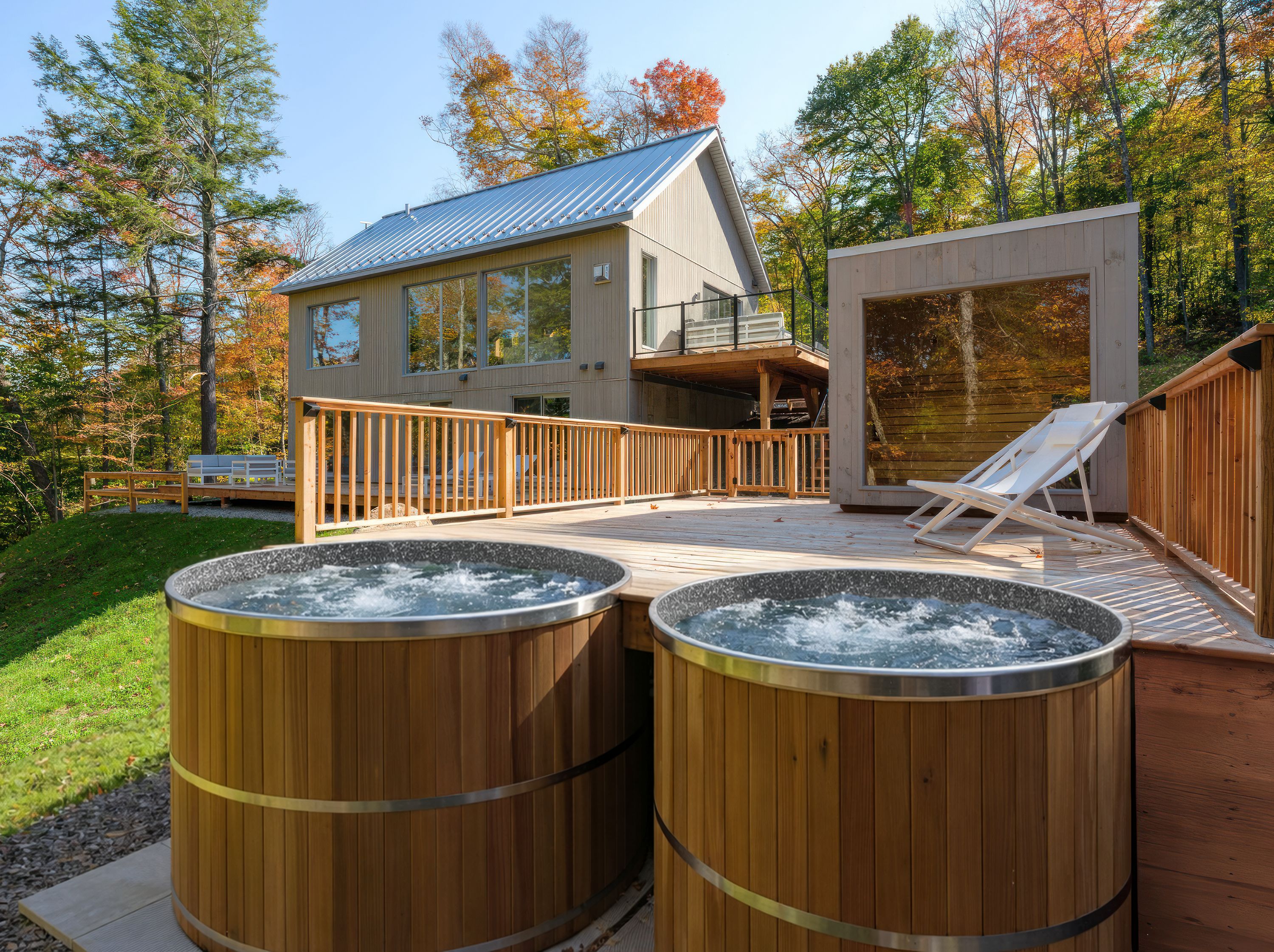 A modern house with a deck, two hot tubs, and a lounge chair.