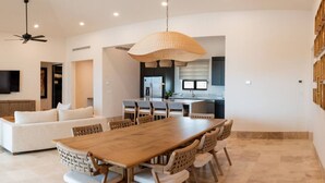 Een moderne woonkamer met een houten eettafel en stoelen, een bank en een keuken op de achtergrond.