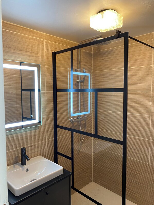 A modern bathroom with a glass-enclosed shower, a white sink, and a mirror with a light above it.