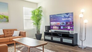 A living room with a sofa, coffee table, potted plant, and a flat-screen TV displaying a streaming service interface. - New & Modern Home in Southport • Family & Pet Friendly (Southport)