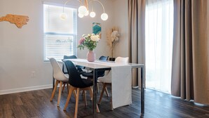 A dining area with a table, chairs, a vase of flowers, and a window with curtains. - New & Modern Home in Southport • Family & Pet Friendly (Southport)