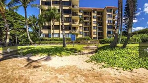 A multi-story hotel with balconies, surrounded by palm trees and a sandy beach area.