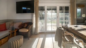 A living room with a sofa, a wicker chair, a striped ottoman, a wooden table, and a TV mounted on the wall. - Beautiful home in Nykøbing Sj with sauna (Nykøbing Sj)