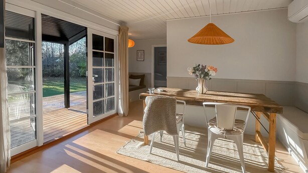 A dining area with a wooden table, white chairs, a woven chair, and a hanging light fixture. - Beautiful home in Nykøbing Sj with sauna (Nykøbing Sj)