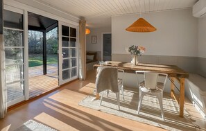 A dining area with a wooden table, white chairs, a woven chair, and a hanging light fixture. - Beautiful home in Nykøbing Sj with sauna (Nykøbing Sj)