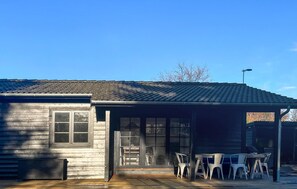 A wooden cabin with a tiled roof, a porch with outdoor seating, and a large window. - Beautiful home in Nykøbing Sj with sauna (Nykøbing Sj)