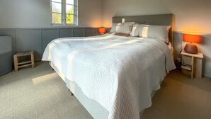 A neatly made bed with a headboard, two bedside lamps, a small wooden stool, and a window with daylight coming through. - Beautiful home in Nykøbing Sj with sauna (Nykøbing Sj)