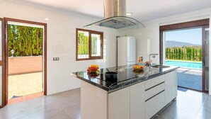 Una cocina moderna con una isla central, horno empotrado y vistas a una piscina.