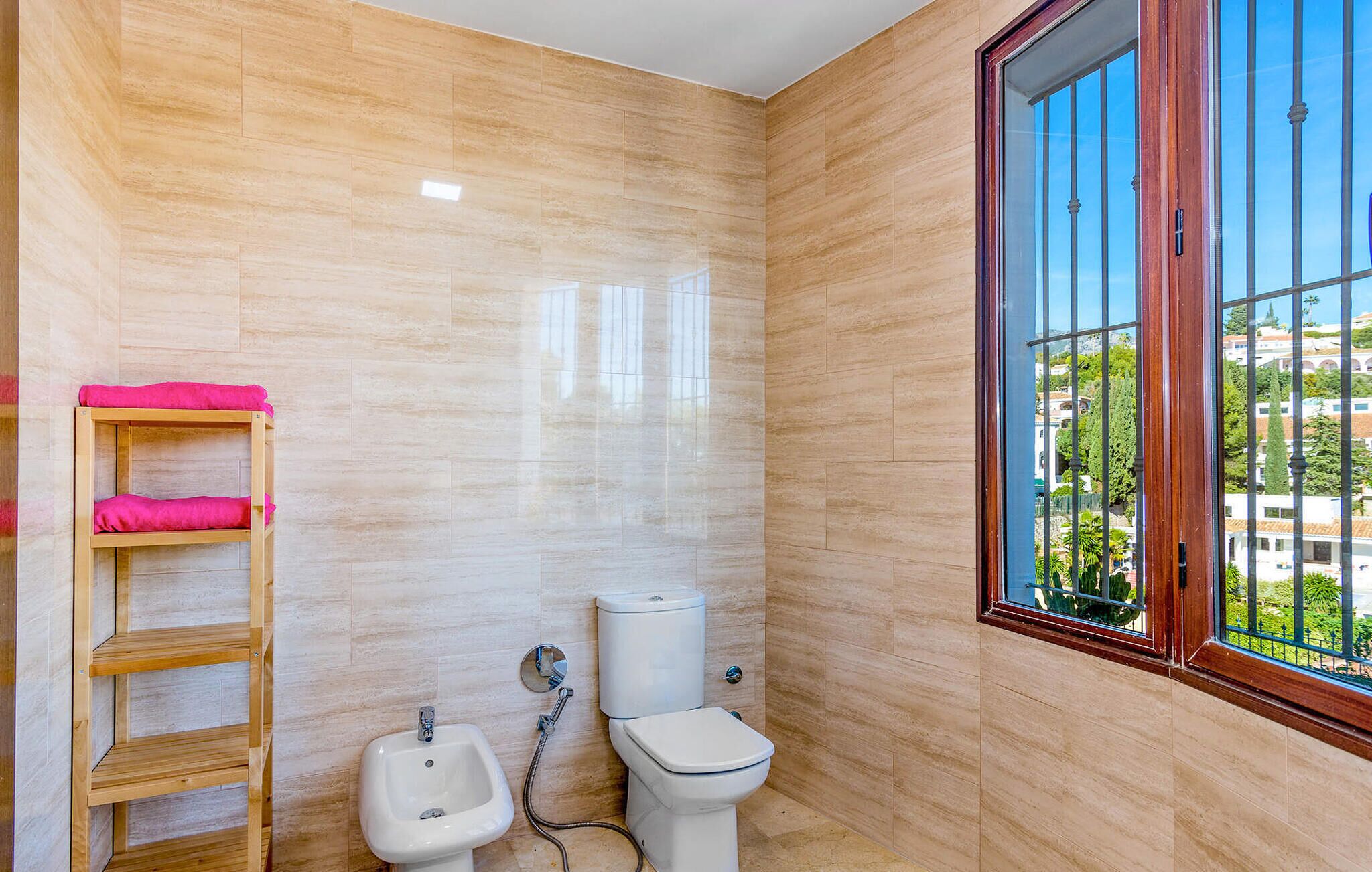 A bathroom with a toilet, bidet, and wooden shelf with towels.