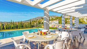 Zona de comedor junto a la piscina con vistas a una montaña y una piscina.