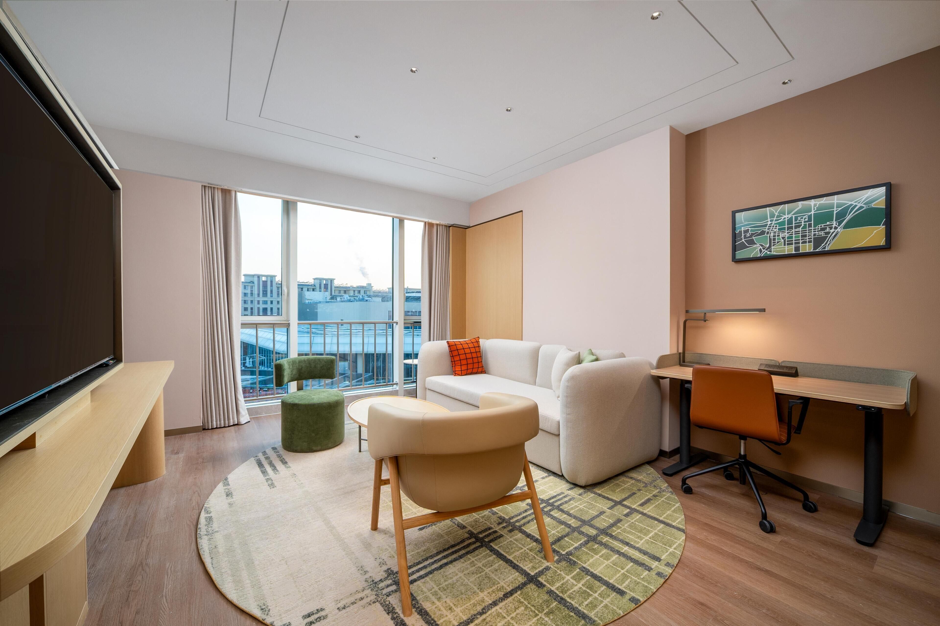 Una habitación de hotel moderna con un ventanal grande, un sofá, un escritorio y un televisor.
