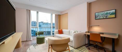 Una habitación de hotel moderna con un ventanal grande, un sofá, un escritorio y un televisor.