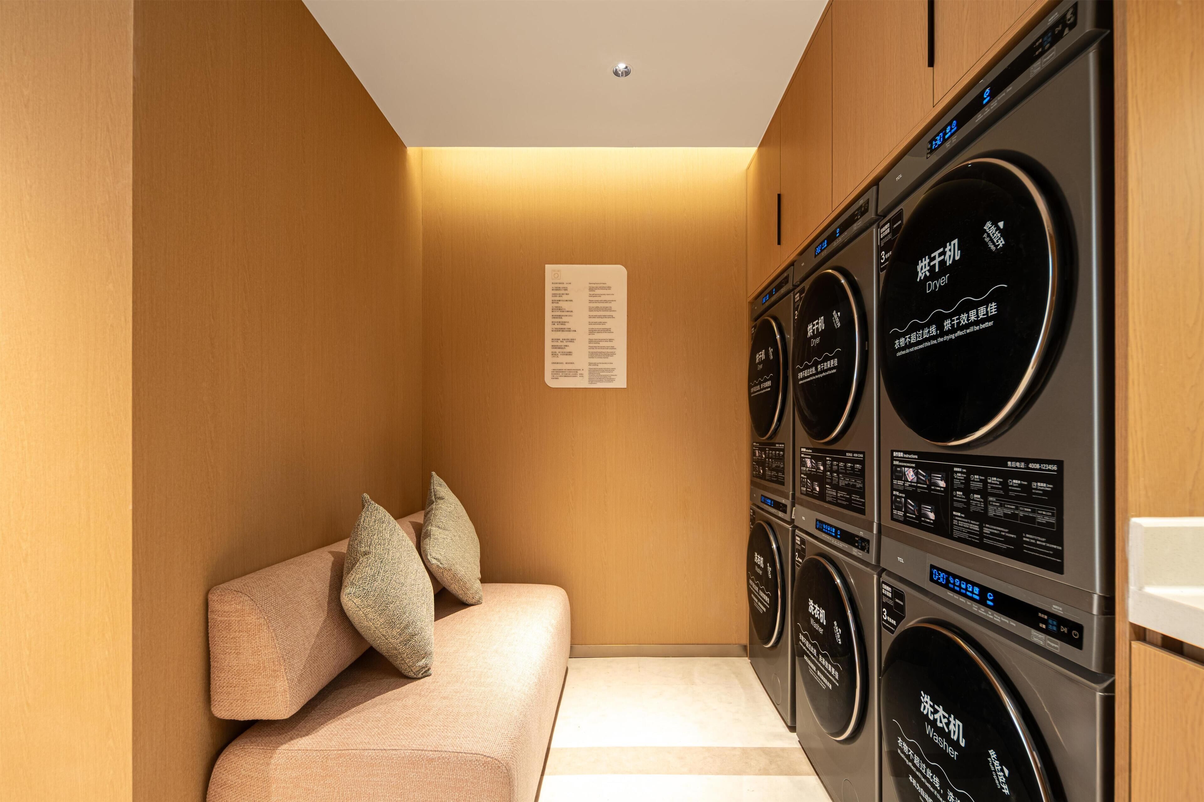 A laundry room with a beige sofa and pillows, and multiple stacked washing machines.