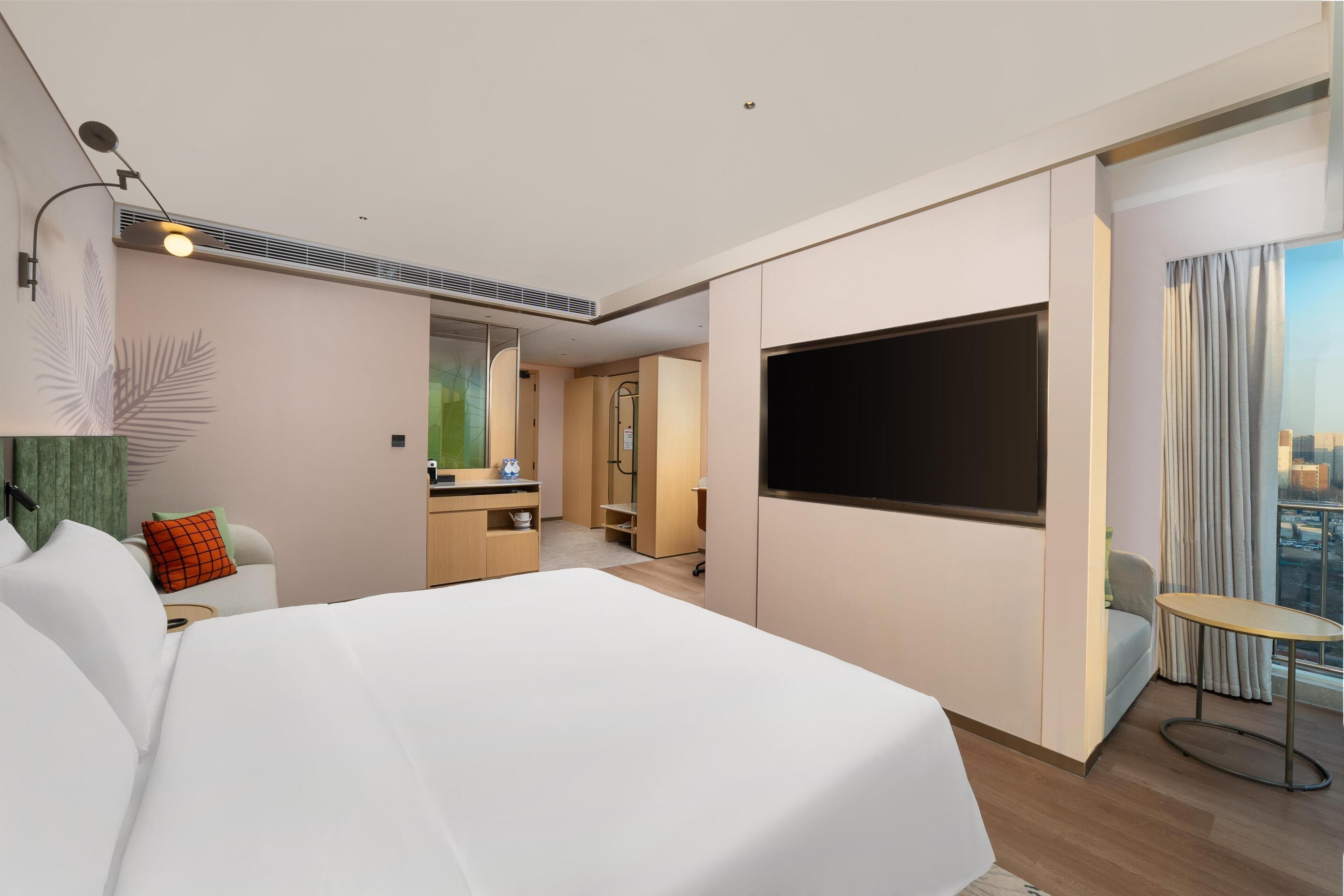 Una habitación de hotel moderna con una cama grande, un televisor de pantalla plana, un escritorio pequeño y vistas de la ciudad a través de la ventana.