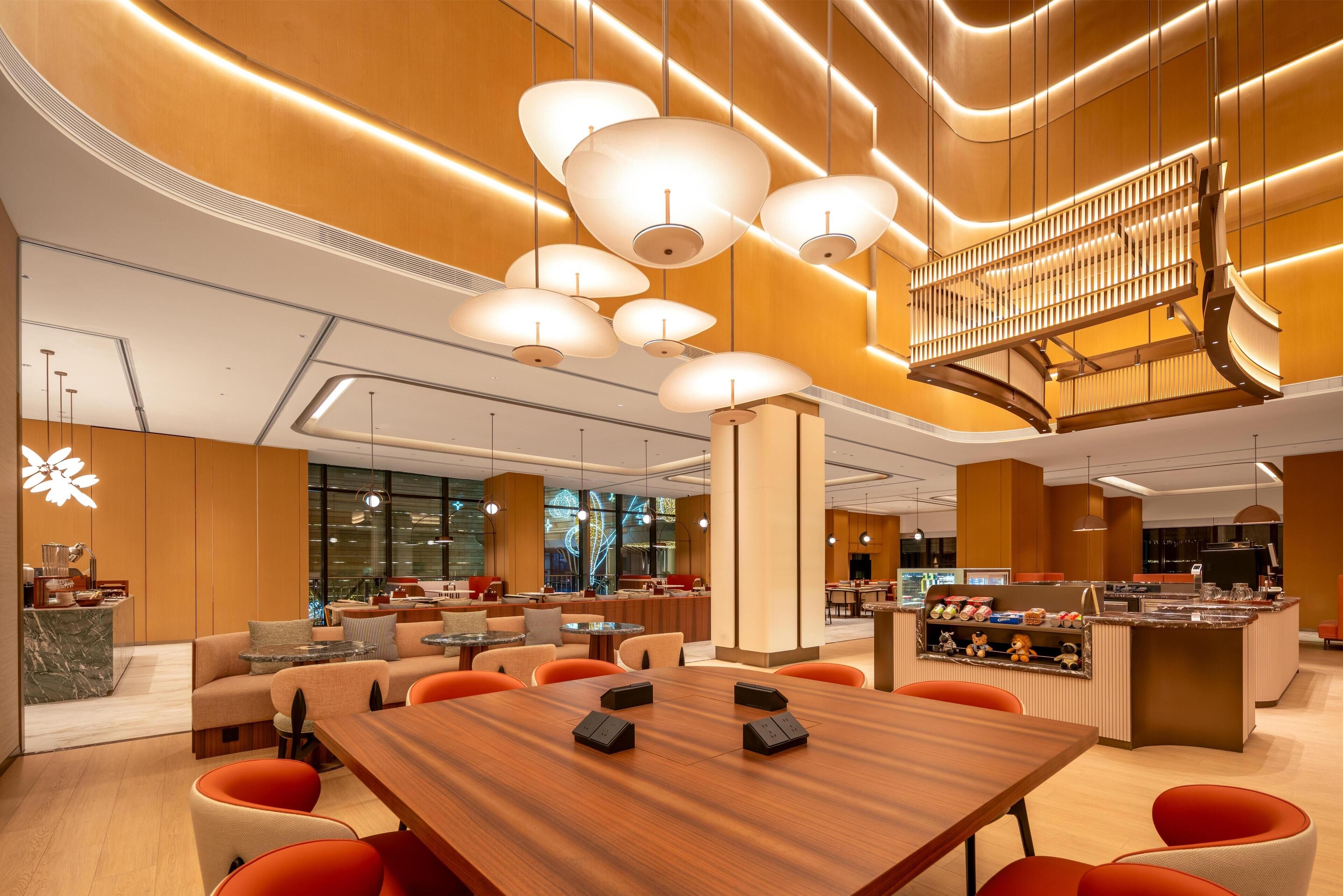 A modern hotel lobby with a wooden reception desk, multiple seating areas, and a central conference table.