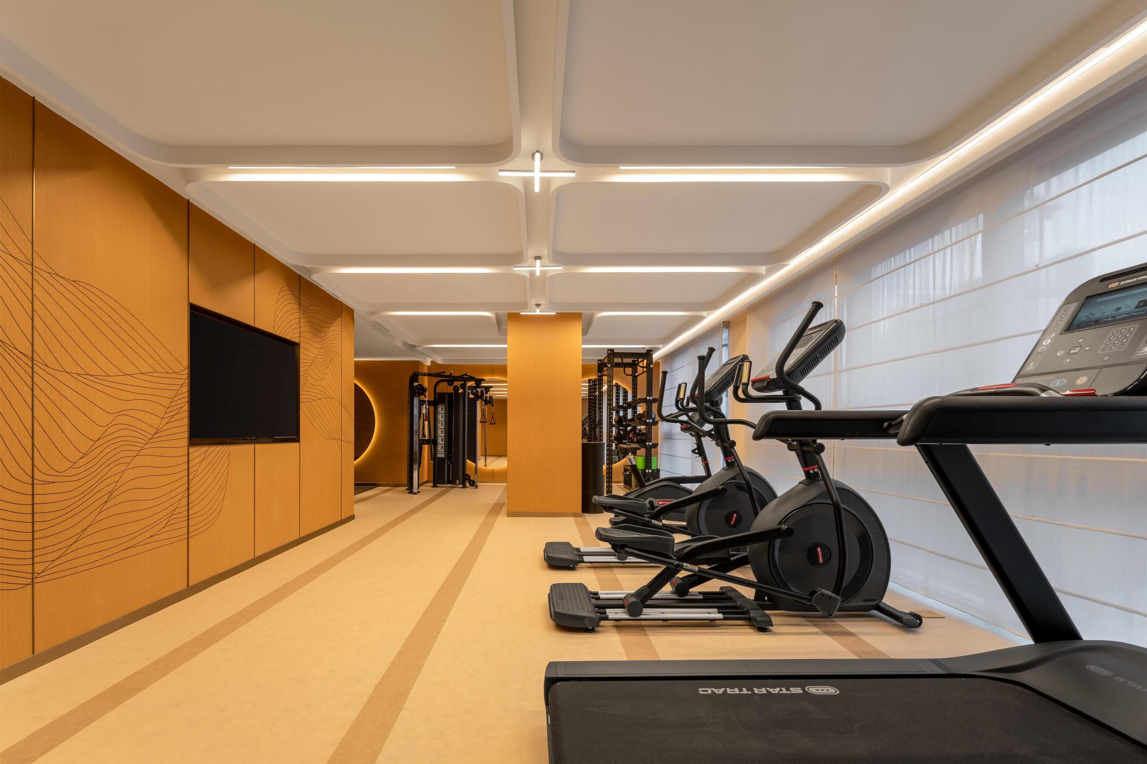 Une salle de sport équipée de tapis de course, de vélos elliptiques et de matériel de musculation.