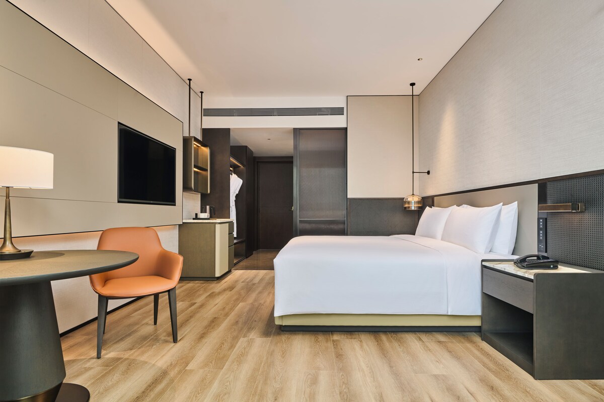 A modern hotel room with a bed, a desk, a chair, and a TV.