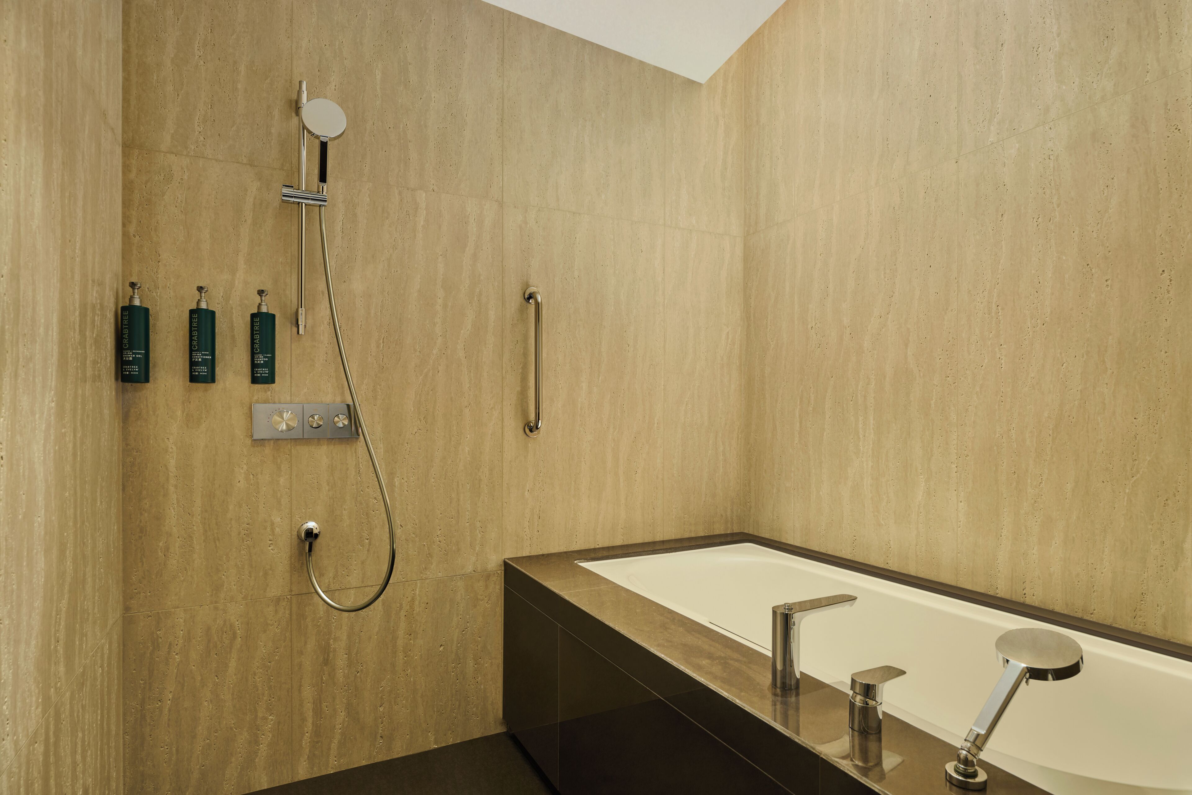A modern bathroom with a large bathtub, a showerhead, and three bottles of shampoo.
