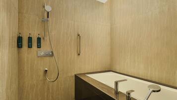 A modern bathroom with a large bathtub, a showerhead, and three bottles of shampoo.