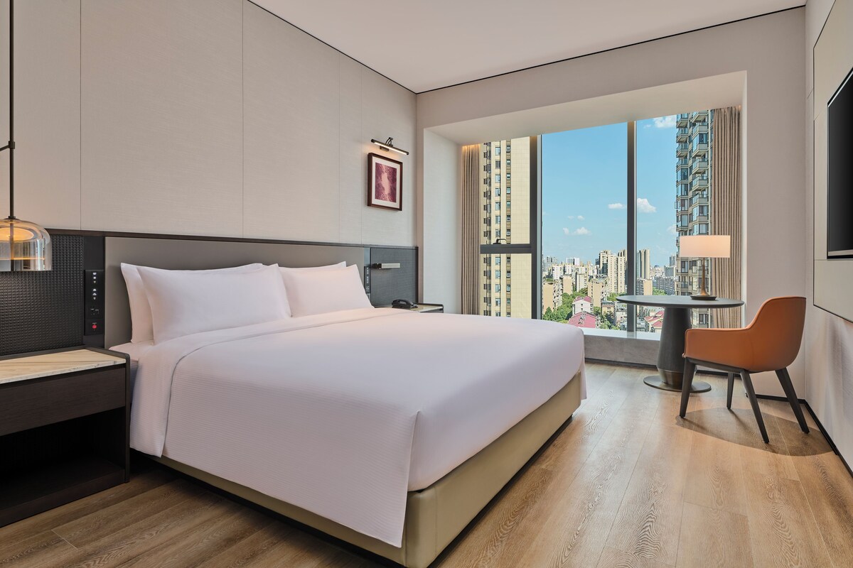 Une chambre d’hôtel moderne avec un grand lit, un bureau, une chaise et une vue sur la ville.