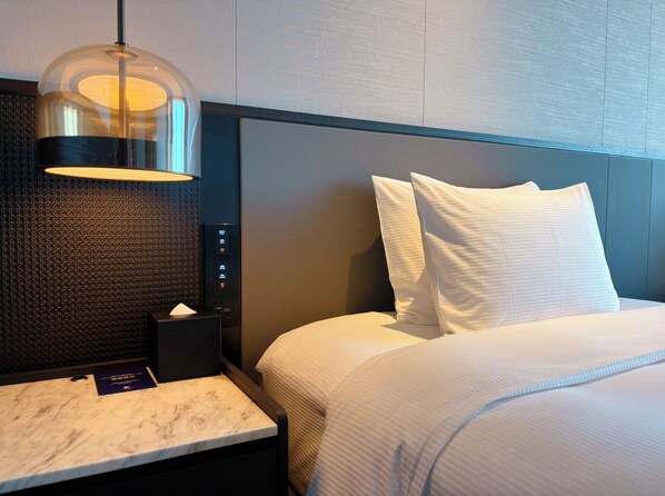 A hotel room with a bed, a nightstand with a lamp, and a marble-topped table. - Doubletree By Hilton Changsha Tianxin (Changsha)