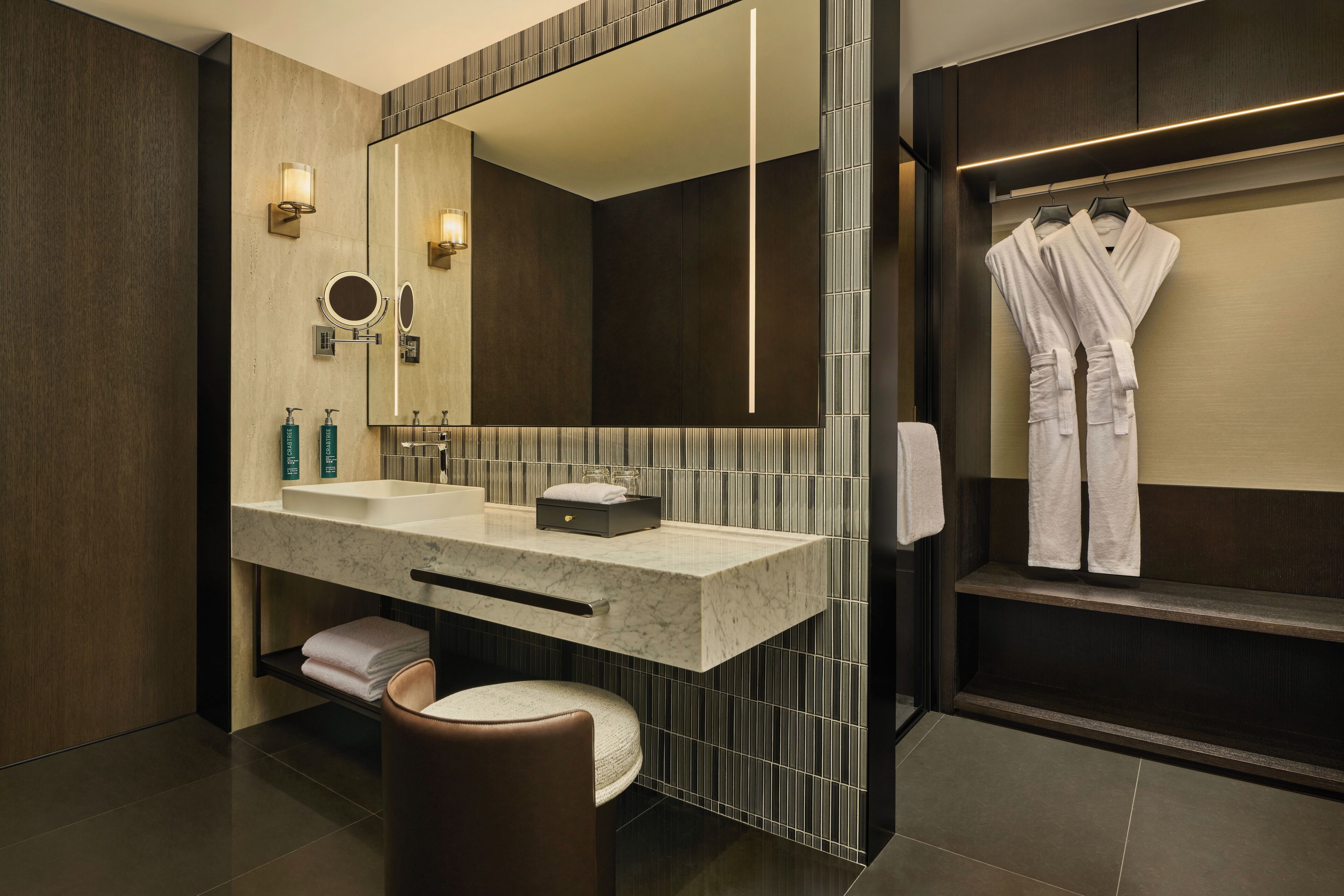 A modern bathroom with a large mirror, two sinks, a vanity, and a robe rack.