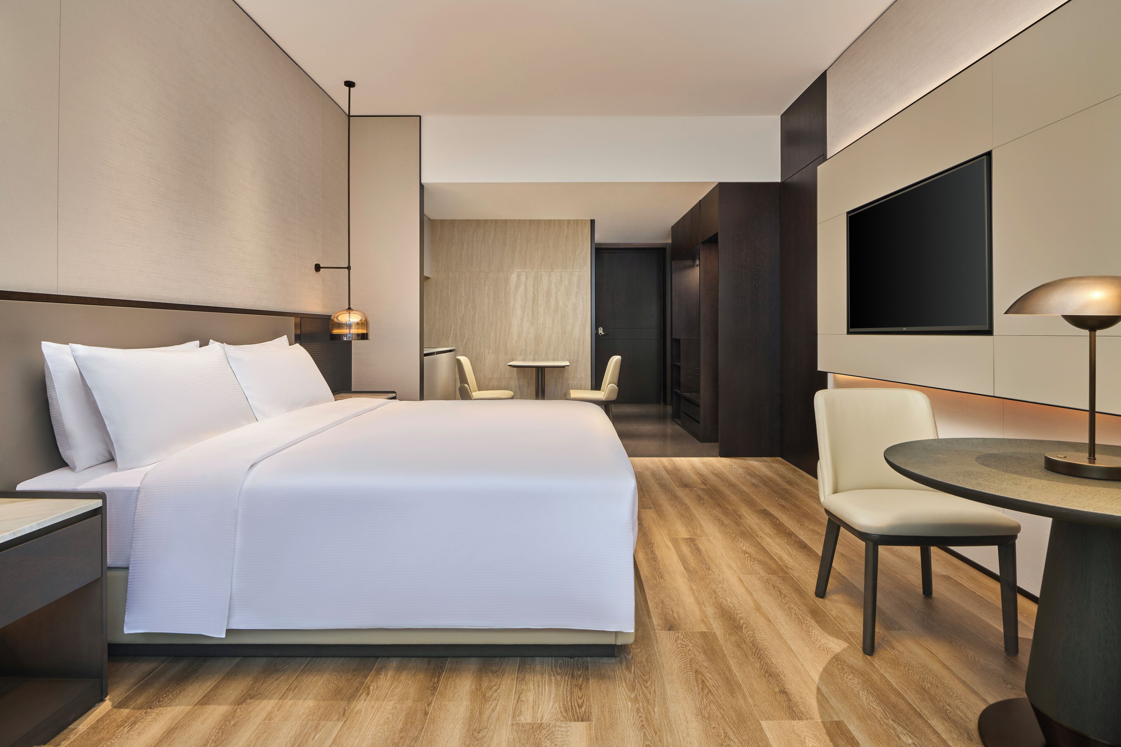 Une chambre d’hôtel moderne avec un grand lit, une petite table ronde, un téléviseur et un coin salon avec des fauteuils.