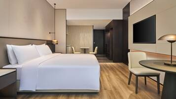 Une chambre d’hôtel moderne avec un grand lit, une petite table ronde, un téléviseur et un coin salon avec des fauteuils.