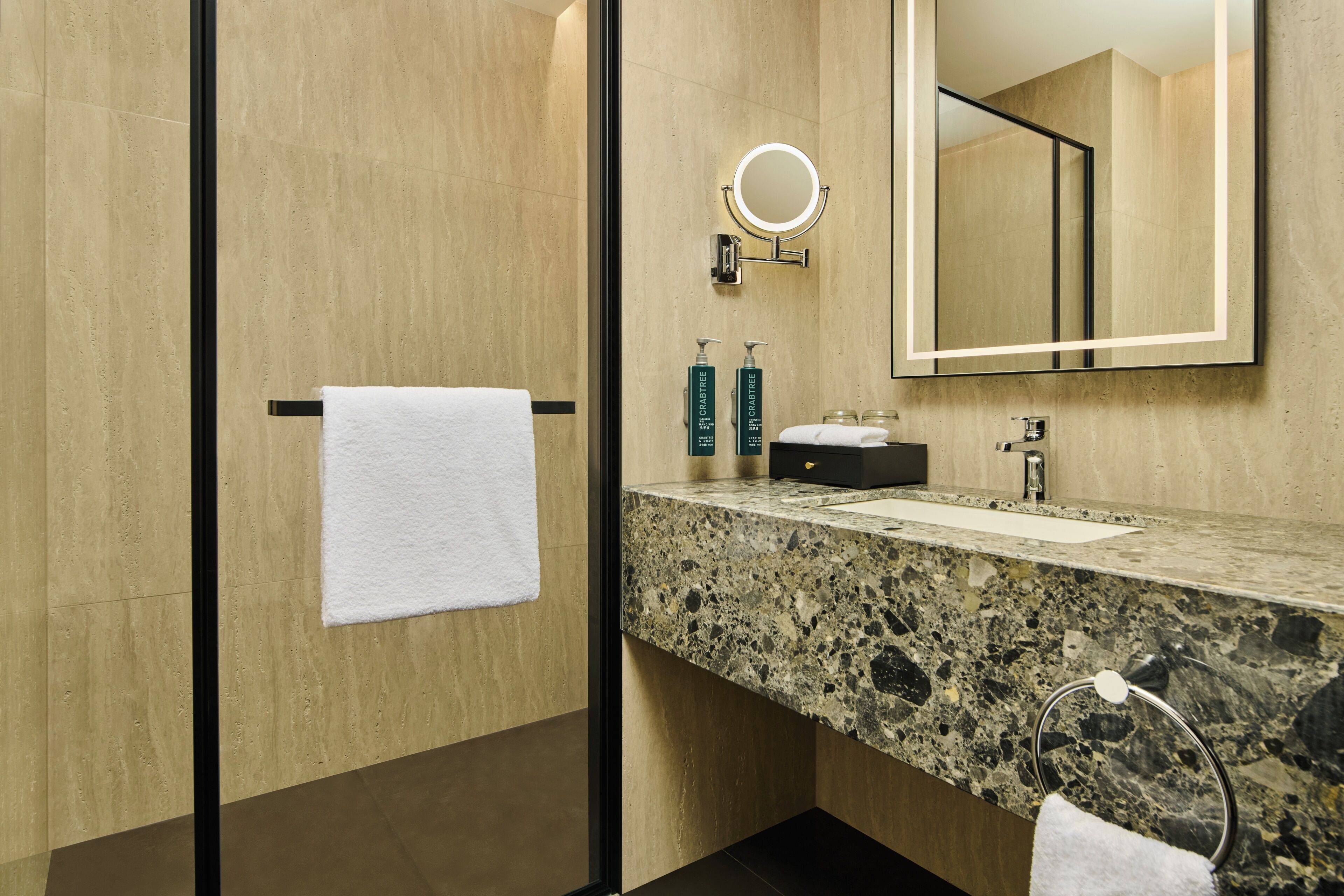 A modern bathroom with a granite countertop, a large mirror, and two bottles of shampoo.
