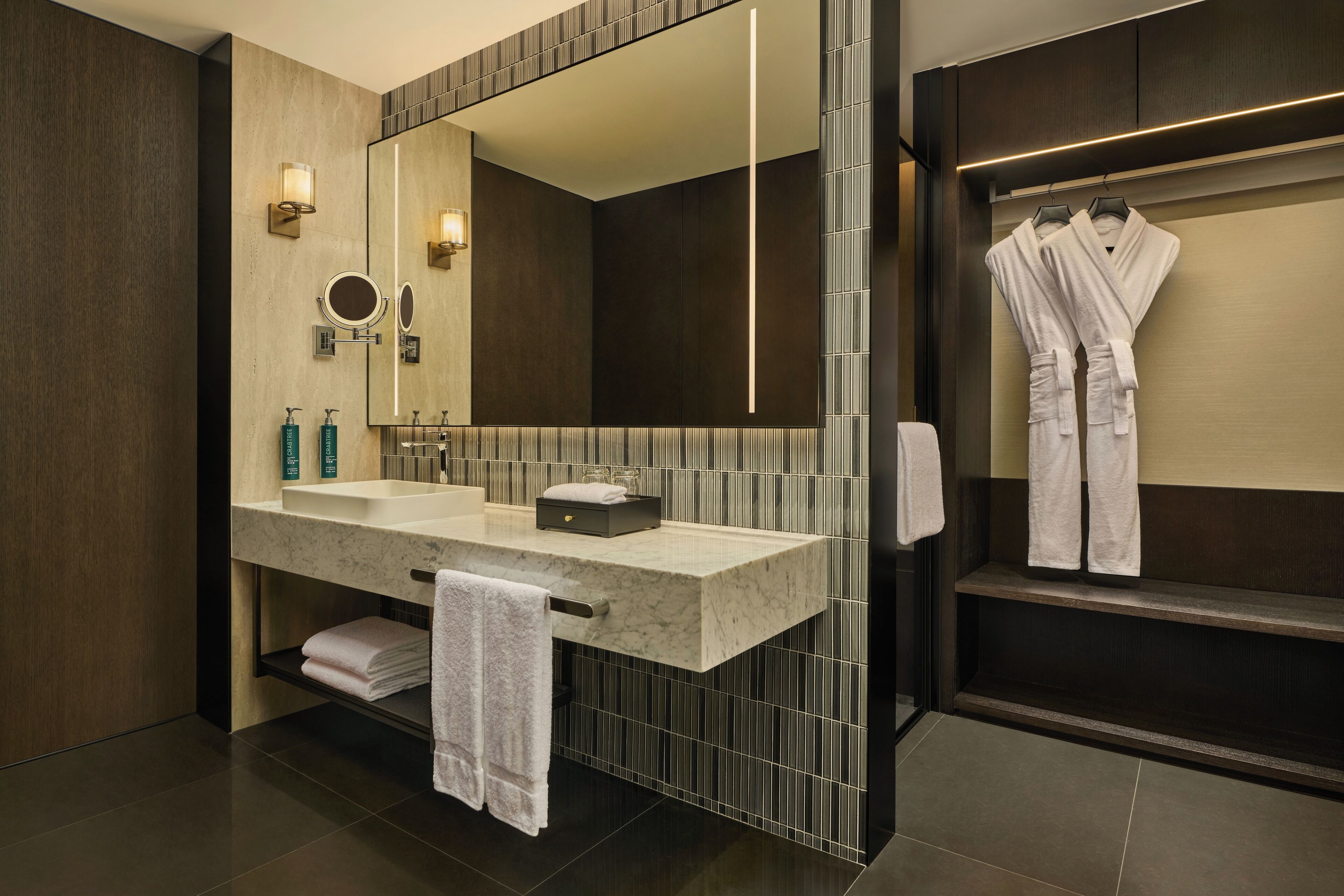 A modern bathroom with a large mirror, two sinks, and a robe rack.
