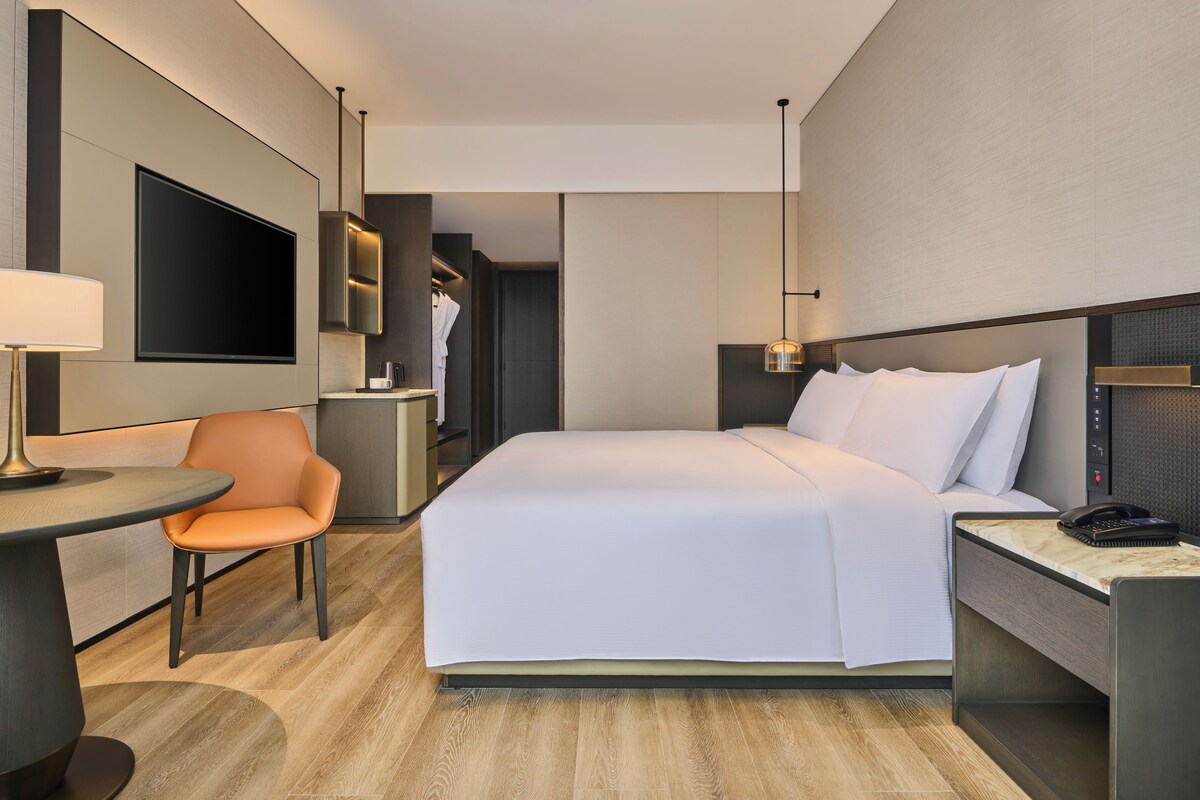 A hotel room with a bed, a desk, a chair, a TV, and a wardrobe.