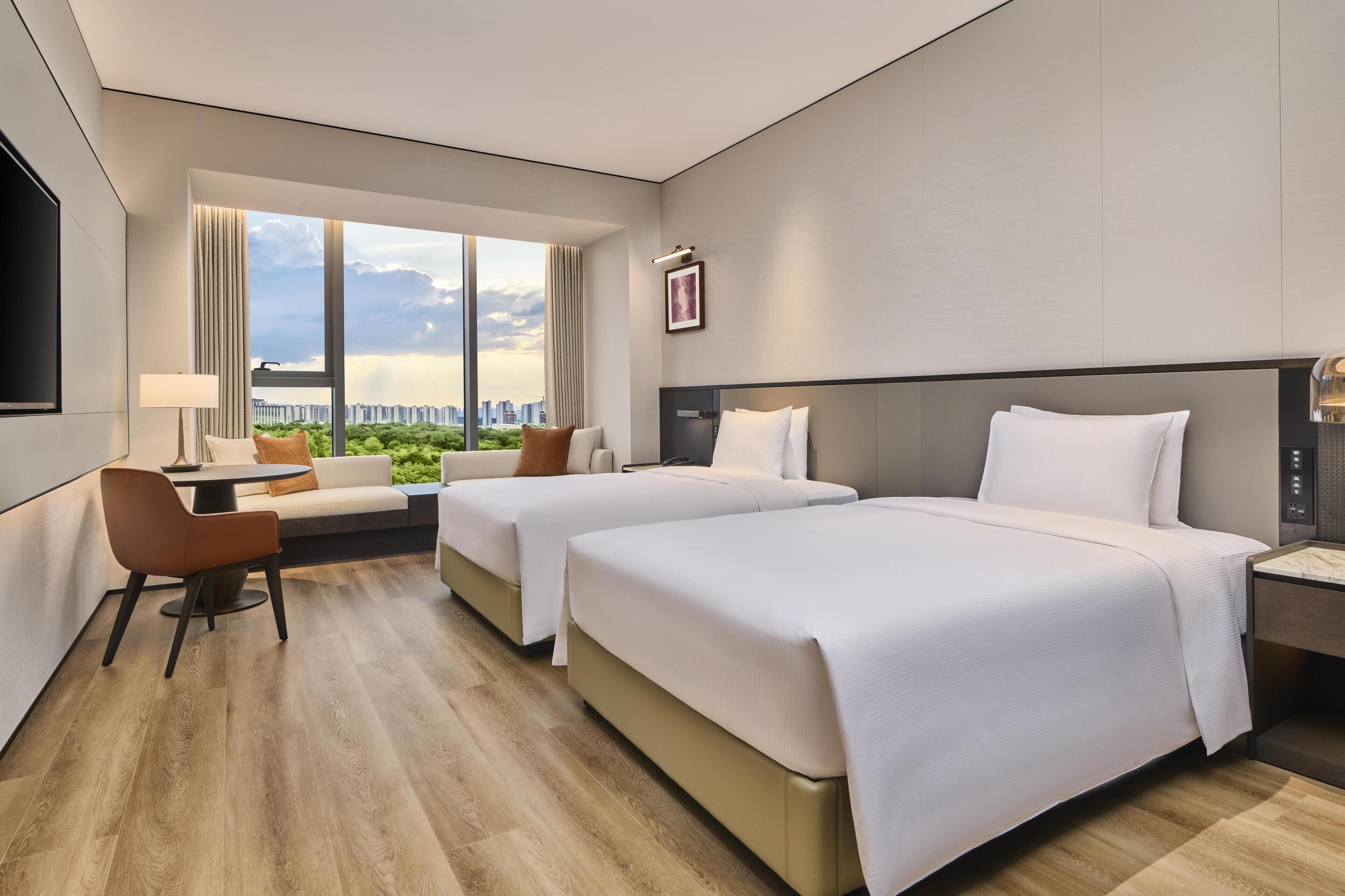 A hotel room with two beds, a sofa, a TV, and a city view.