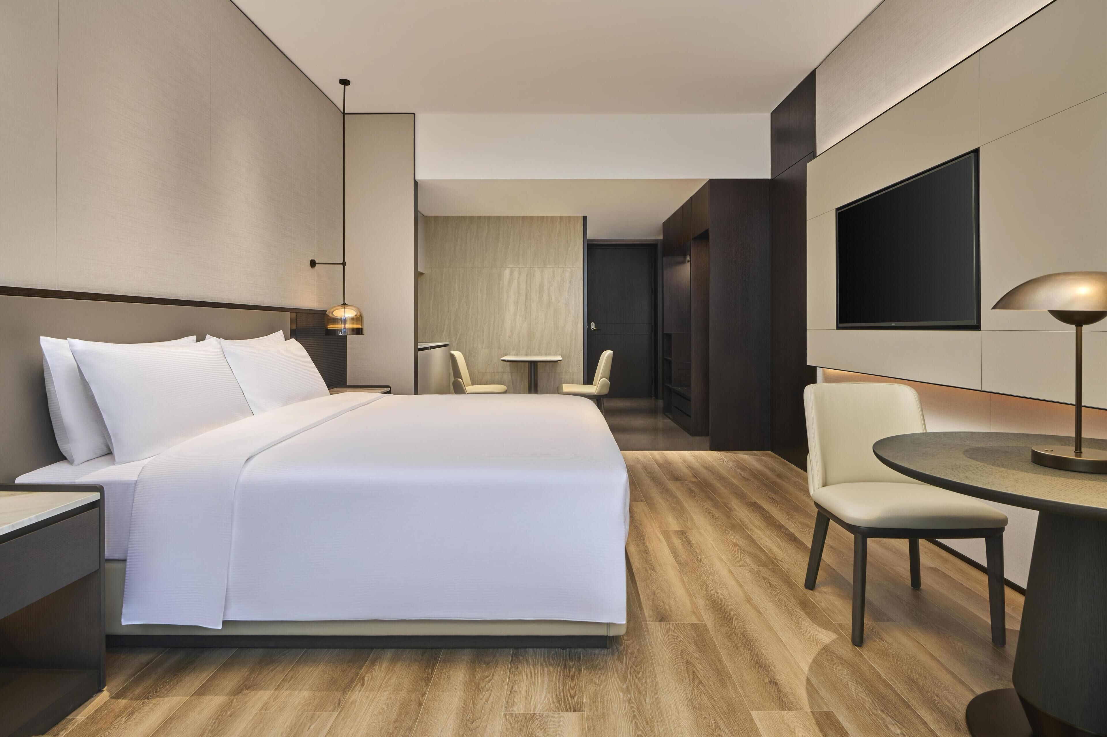 Une chambre d’hôtel moderne équipée d’un grand lit, d’un bureau, d’une chaise, d’une télévision et d’une lampe.
