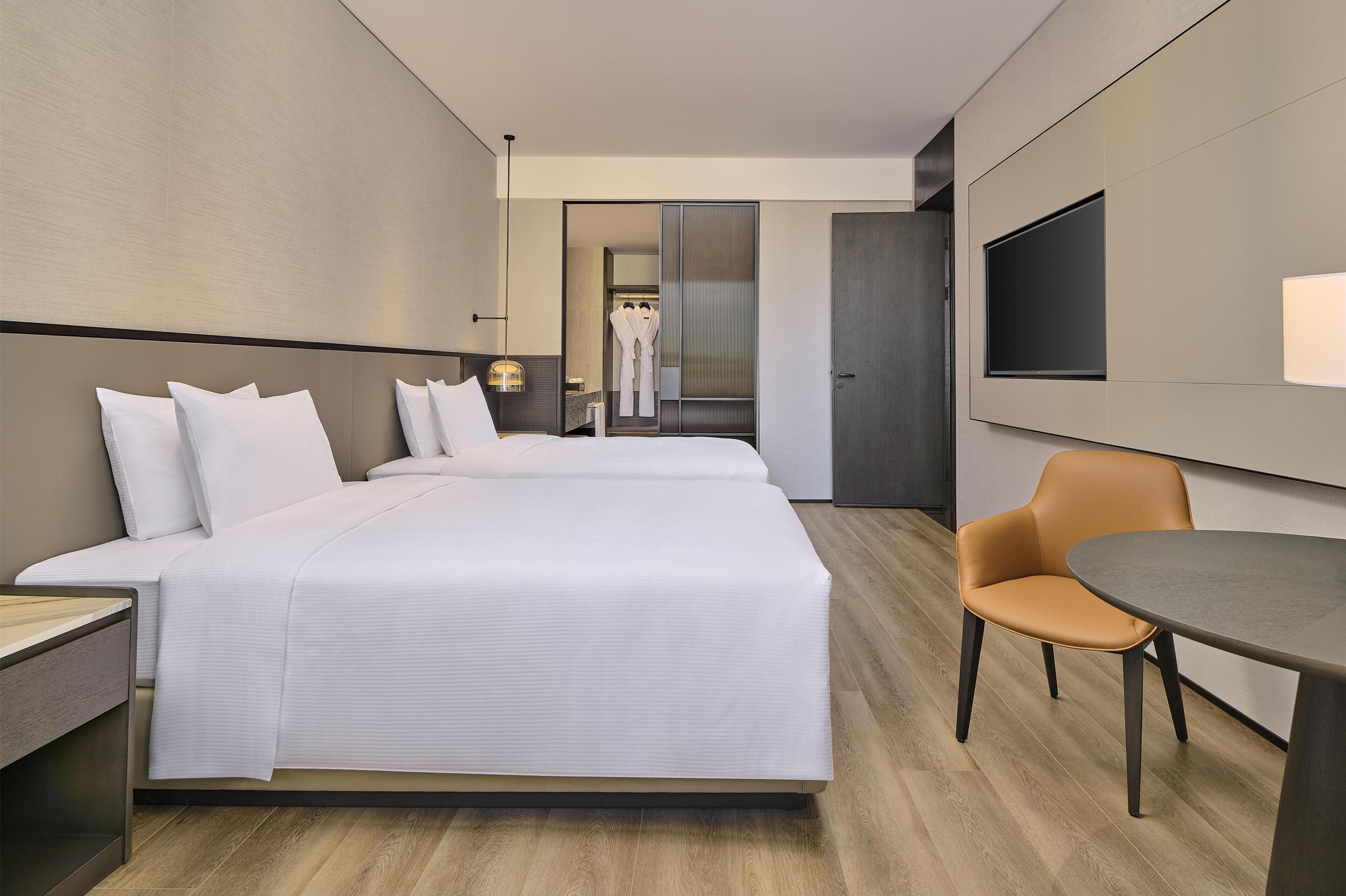 A modern hotel room with a large bed, a desk, a chair, and a flat-screen TV.