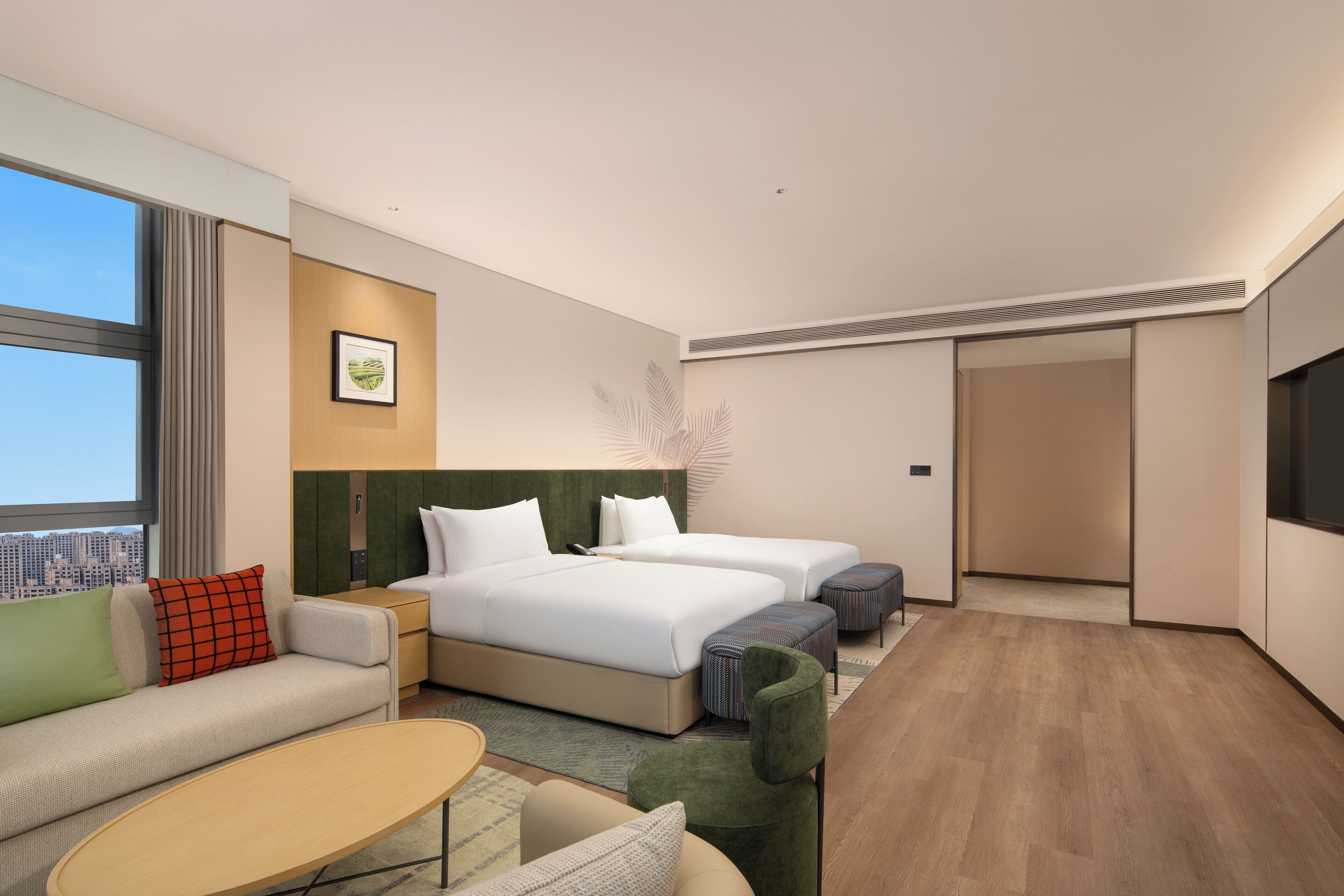 A hotel room with two beds, a sofa, a coffee table, a TV, and a city view.