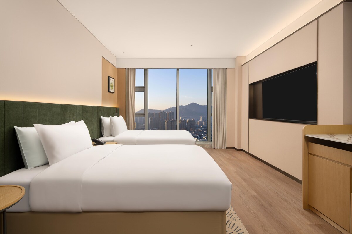 A hotel room with two beds, a TV, and a city view.