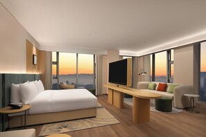 Une chambre d’hôtel moderne dotée d’un grand lit, d’une télévision à écran plat, d’un canapé, d’un bureau et d’une grande fenêtre donnant sur la ville.