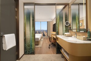 A modern hotel room with a city view, a large bed, a desk, and a bathroom with a large mirror.