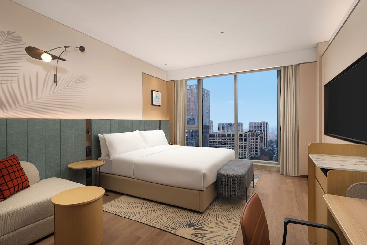 Ein modernes Hotelzimmer mit einem großen Bett, einem Schreibtisch, einer Couch, einem kleinen Tisch und einem Fernseher.