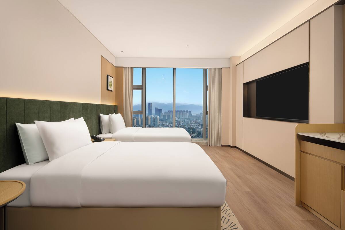 Ein Hotelzimmer mit einem großen Bett, einem Fernseher und Blick auf die Stadt.