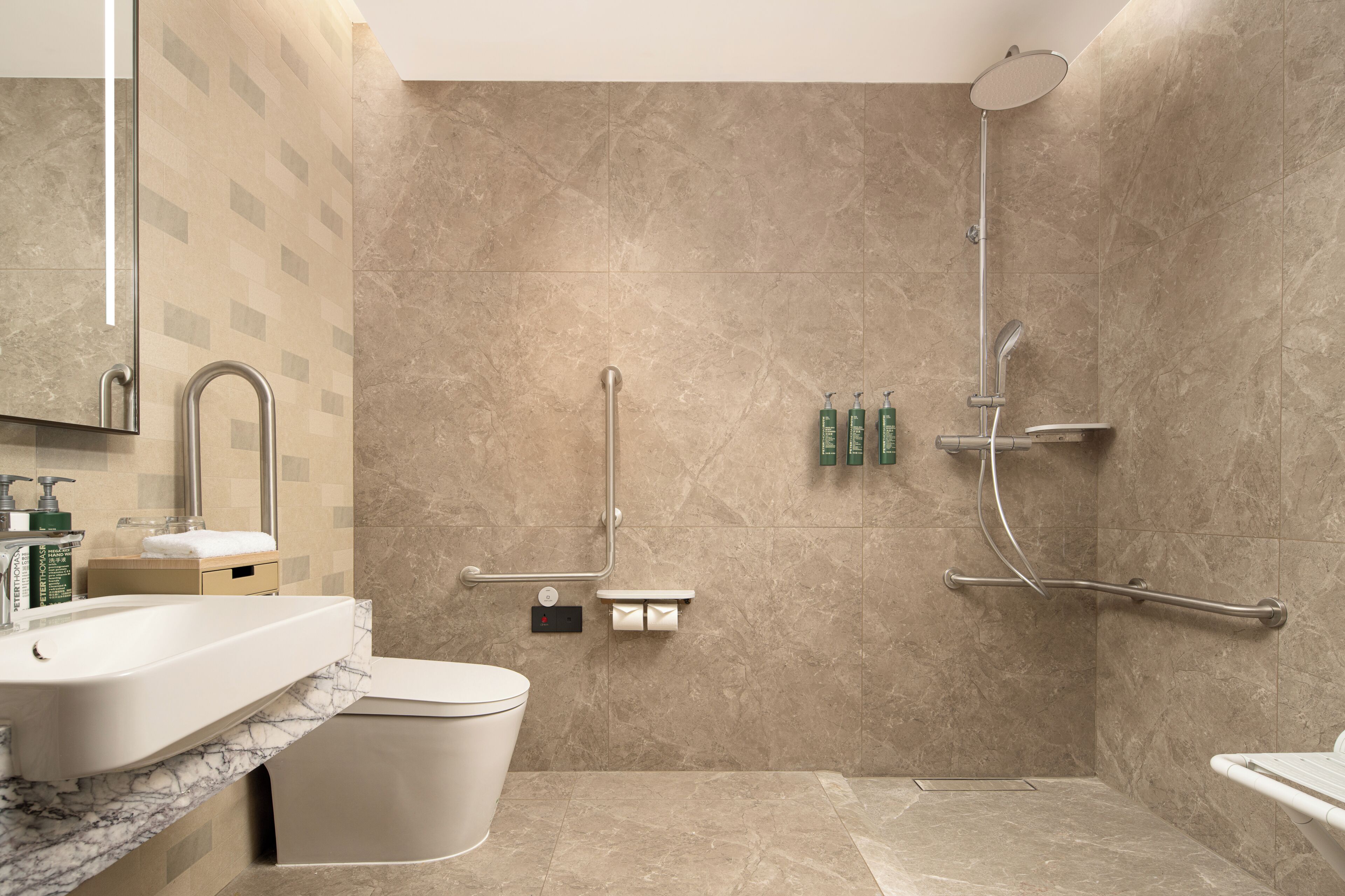 A modern bathroom with a marble sink, a toilet, a shower with a handheld showerhead, and grab bars.