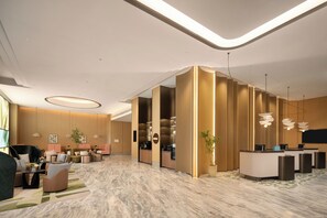 Un hall d’hôtel moderne comprenant des espaces de détente, un comptoir d’accueil et une zone de réception.